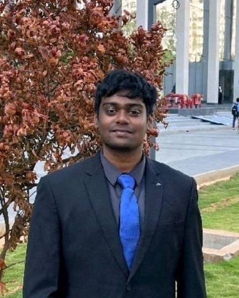 Shrinidhi KJ in a dark suit and blue tie, standing outdoors